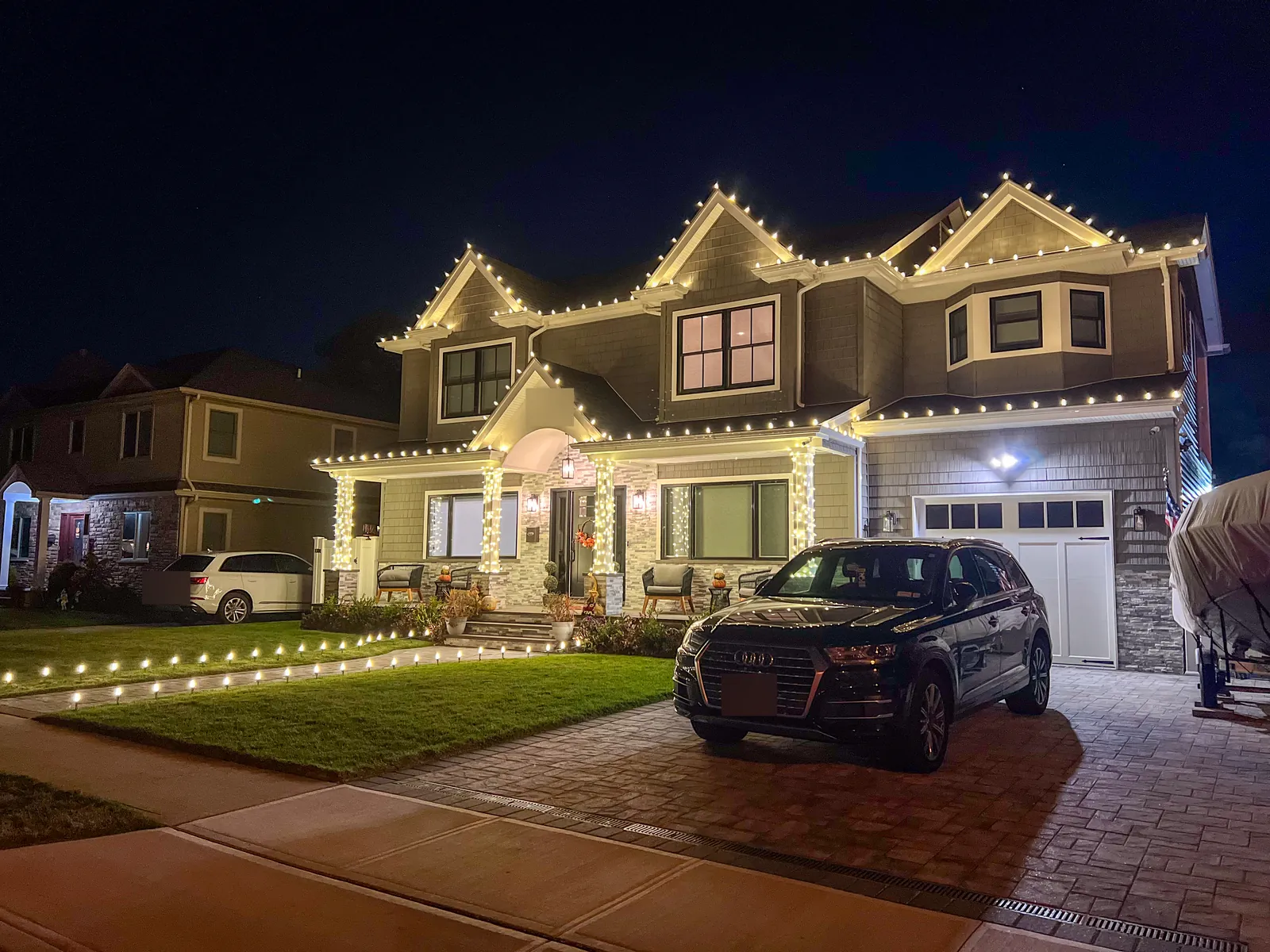 Craftsman style home in Albertson with warm white roofline lights on every gable, wrapped porch columns and lawn stake lights