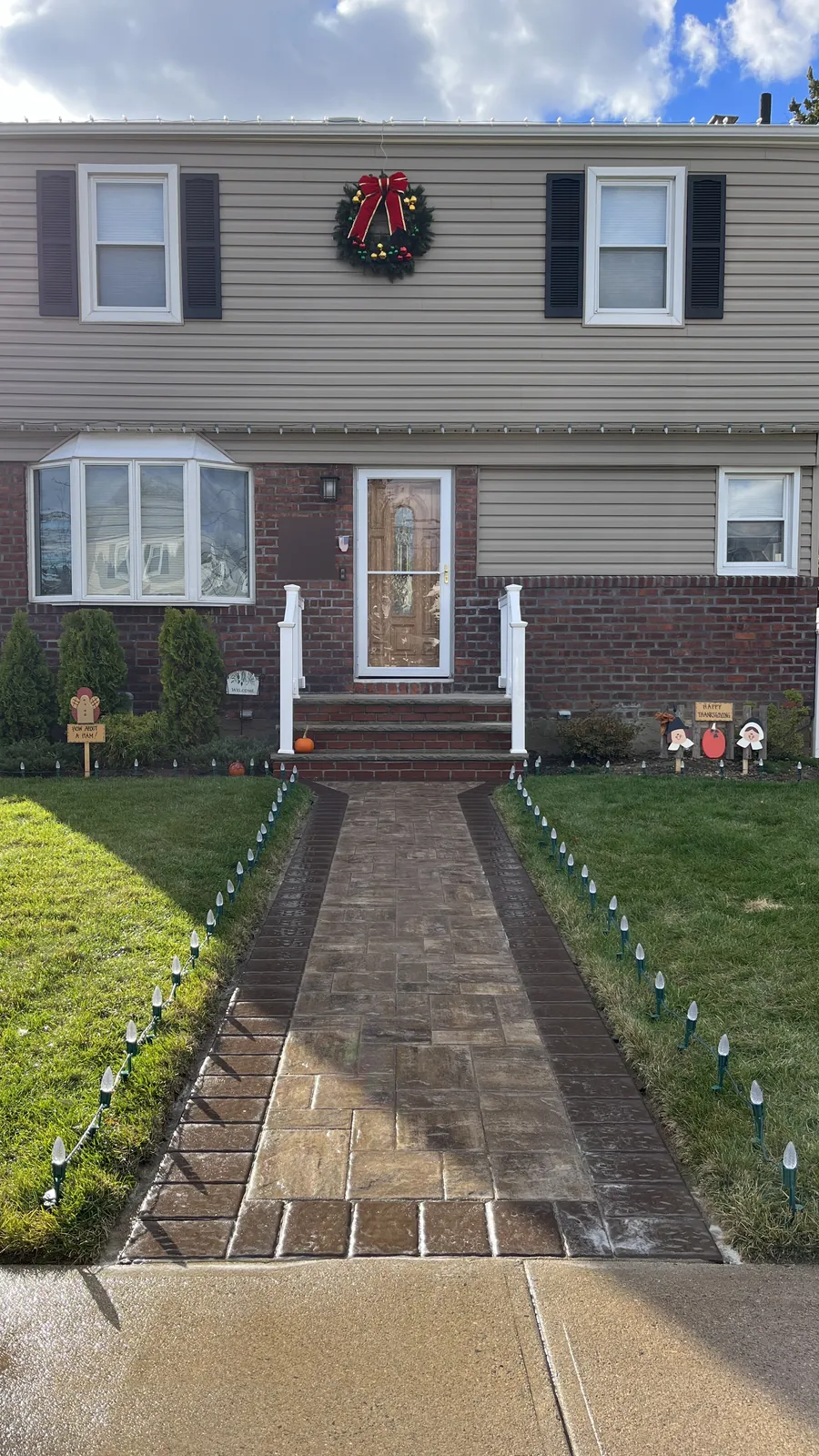Daytime view of a finished Christmas light install in Mineola with roofline bulbs, a wreath and walkway stakes