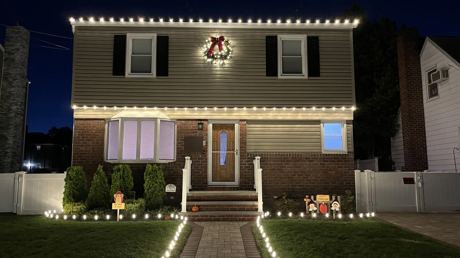 Warm white C9 roofline lights, a lit wreath and walkway stake lights on a two story home in Mineola at night