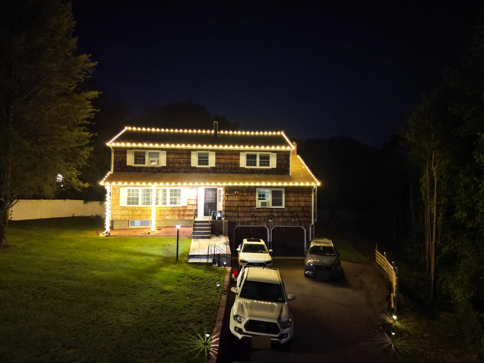 Drone view at night of warm white roofline Christmas lights on a colonial home in Smithtown